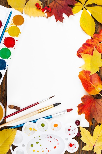 Komposition mit Blatt weißem Papier malt Pinsel und bunte Blätter im Herbst