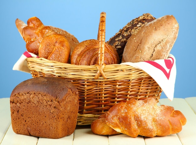 Komposition mit Brot und Brötchen im Weidenkorb auf Holztisch auf farbigem Hintergrund