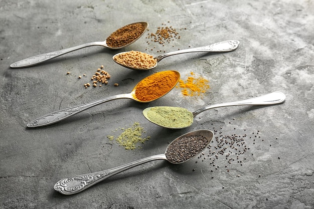 Komposition mit einer Auswahl an Superfood-Produkten in Löffeln auf grauem, strukturiertem Hintergrund