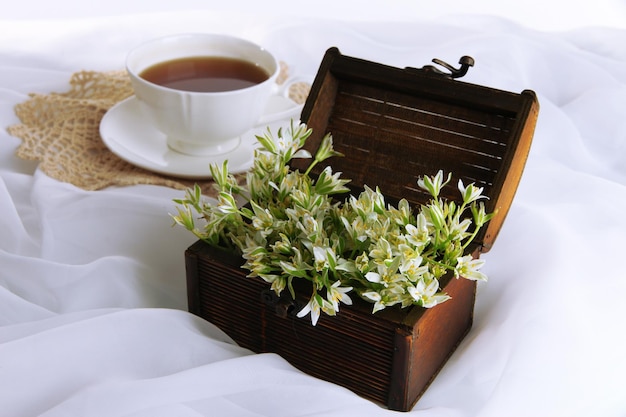 Komposition mit Frühlingsblumen und Tasse Tee auf weißem Satinhintergrund