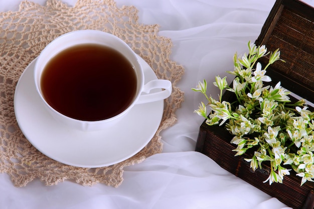 Komposition mit Frühlingsblumen und Tasse Tee auf weißem Satinhintergrund