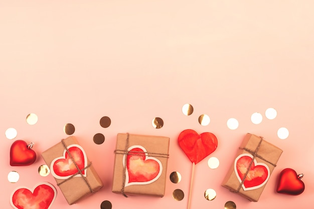 Komposition mit Geschenkboxen, Glasherzen, Lollypop und Goldkonfetti auf Pink. Hintergrund mit Kopienraum für Valentinstag.