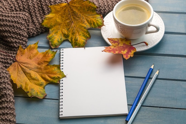 Komposition mit Herbstlaub leere Notizbücher eine Tasse Kaffee auf einem blauen Holztisch