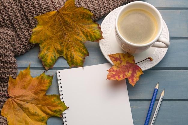 Komposition mit Herbstlaub leere Notizbücher eine Tasse Kaffee auf einem blauen Holztisch