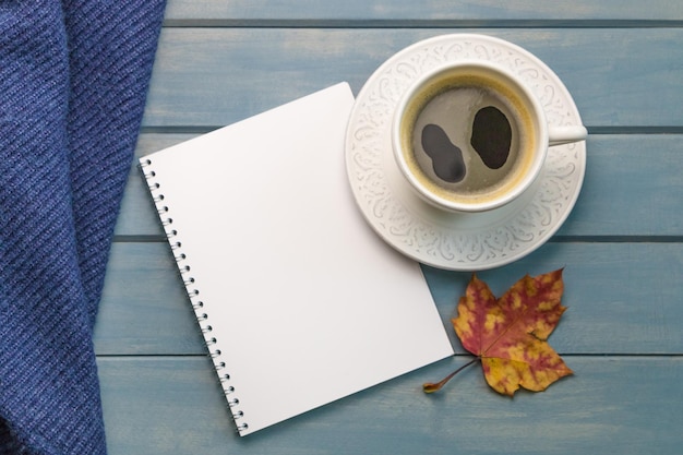 Komposition mit Herbstlaub leere Notizbücher eine Tasse Kaffee auf einem blauen Holztisch