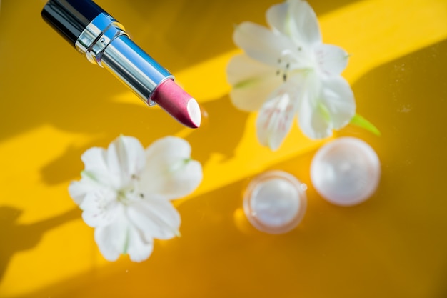 Komposition mit Lippenstift und Blumen auf gelbem Hintergrund kreative flache Lage aus rosa Lippenstiften und w...