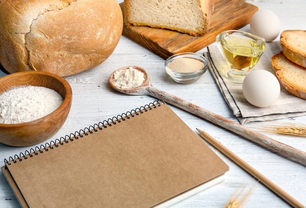 Komposition mit Notizbuch und Zutaten für Brot auf Holztisch