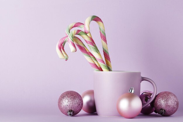 Komposition mit Weihnachtsspielzeug, süße Zuckerstange in einer Tasse auf farbigem Hintergrund