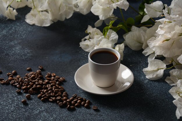 Komposition mit weißer Tasse Kaffee, Bohnen und Blumen als Hintergrund