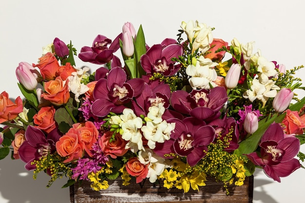 Komposition von Blumen aus rosa Rosen, burgunderroten Orchideen, roten Tulpen, Hyazinthen und Hrzemtem. Blumenarrangement in einer Schachtel für ein Mädchen aus Rosen, Tulpen und Orchideen auf weißem Hintergrund