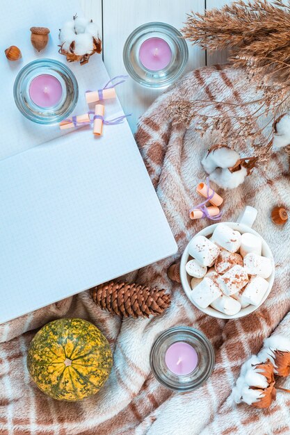 Komposition von oben mit einer Tasse Kaffee und Marshmallow-Kürbiskerzen Baumwollpflanze Blumenzweige Notizblock und Kopierraum Herbst Winter schöner Hintergrund gemütliches Wohnkonzept