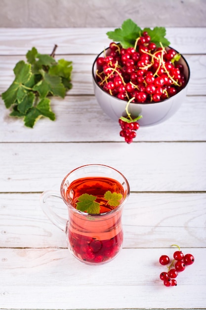 Kompott aus roten Johannisbeeren in einem Glas und einer Beere in einer Schüssel auf dem Tisch Hausgemachte Sommergetränke vertikale Ansicht