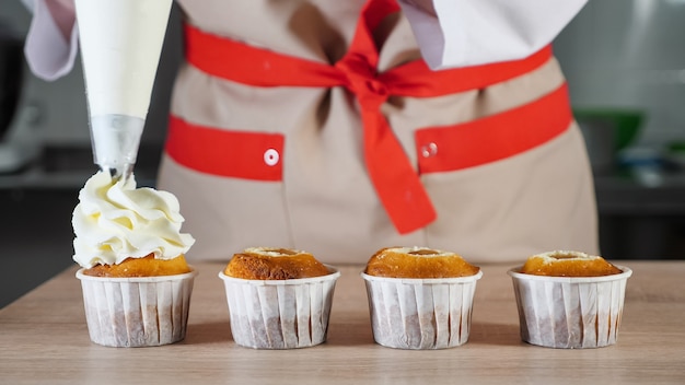 Konditor dekoriert Cupcakes in Pappbechern weiß creme mit Spritzbeutel. Hände Nahaufnahme. Vorderansicht