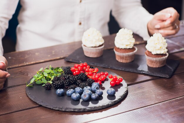 Konditor dekoriert den oberen Cupcake vor dem Servieren mit glasierter Johannisbeere