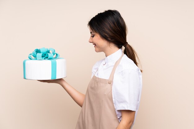 Konditor, der einen großen Kuchen über isolierter Wand hält