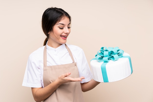 Konditorfrau, die einen großen Kuchen über lokalisierter Wand hält