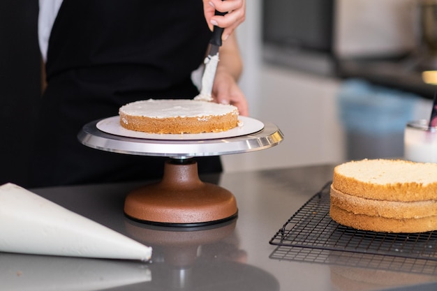 Konditorin schmiert mit einem Messer Sahne um frische Kuchenschichten