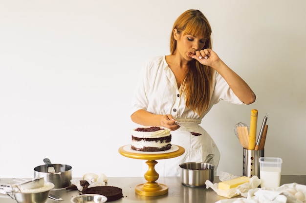 Konditormädchen bereitet einen Kuchenkeks mit weißer Sahne und Schokoladenkuchen vor