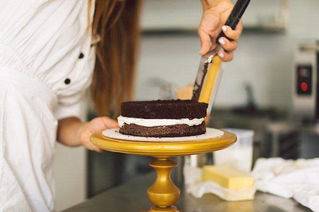 Konditormädchen bereitet einen Kuchenkeks mit weißer Sahne und Schokoladenkuchen vor
