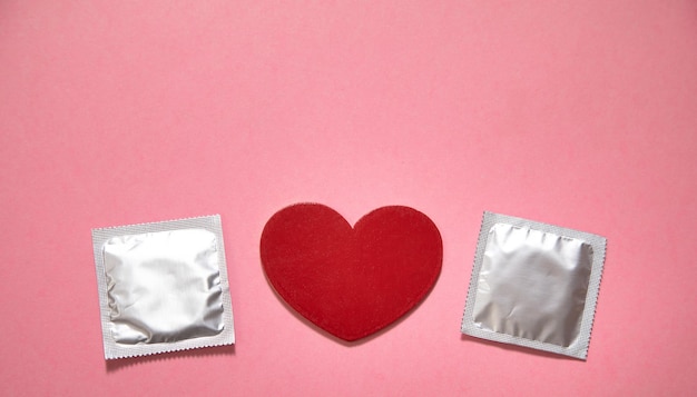 Kondom und rotes Herz auf dem rosa Hintergrund
