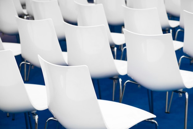 Konferenzstühle in Geschäftsraumreihen aus weißem Kunststoff, bequeme Sitze in leeren Unternehmenspräsentationssitzungen im Bürodetail, selektiver Fokus, blauer Boden
