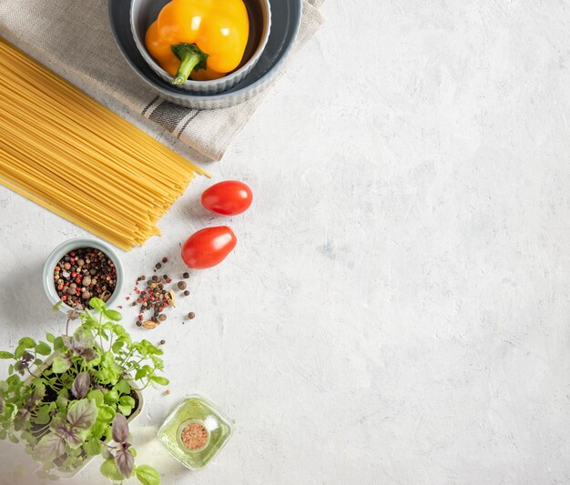 Konsept flach mit rohen Spaghetti mit Tomaten, Basilikum, Pfeffer und Olivenöl auf weißem Backsteinhintergrund. Traditionelle Zutaten für die Herstellung von italienischer Pasta. Draufsicht und Kopienraum.