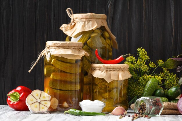 Foto konservierte gurken in gläsern, frische gurken, kräuter und gewürze zur marinade auf holzgrund