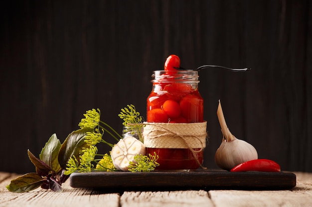 Konservierte Kirschtomaten in einem offenen Gefäß Gewürze und Kräuter für die Marinade auf einem hölzernen Hintergrund