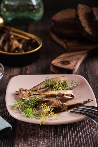 Konservierte Sprat-Fische in Öl und Dill auf einem Teller auf dem Tisch, vertikale Ansicht