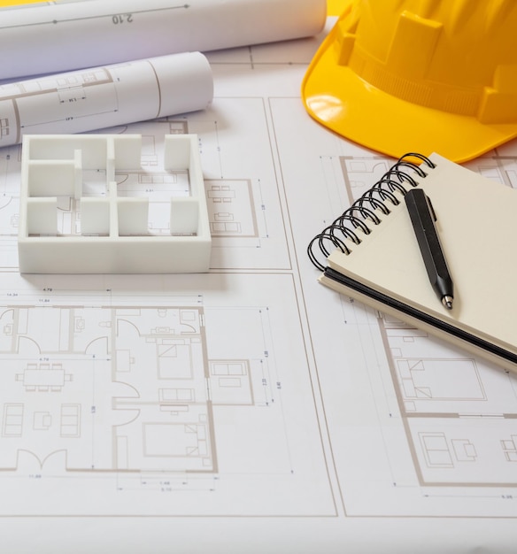 Konstruktionskonzept Wohngebäudezeichnungen und Hardhat auf einem Büroschreibtisch