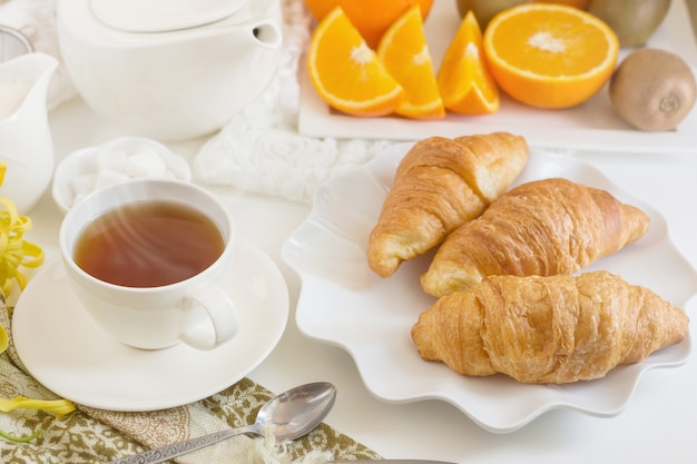 Kontinentales Frühstück mit goldenen französischen Hörnchenfrüchten und Tasse Tee. Frühstückskonzept