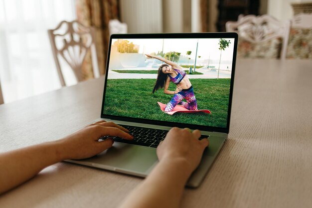 Konzentrieren Sie sich auf den Laptop-Bildschirm mit einer jungen Frau in Sportbekleidung, die Morgenübungen macht und tiefe Kniebeugen auf einer Yogamatte macht, um zu Hause fit zu bleiben