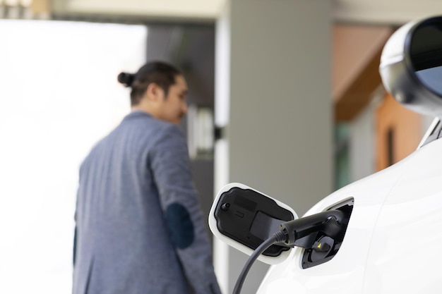 Konzentrieren Sie sich auf die EV-Ladestation zu Hause mit unscharfem, progressivem Mann im Hintergrund