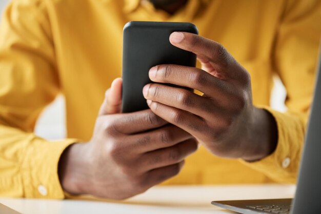 Konzentrieren Sie sich auf die Hände eines jungen afroamerikanischen Angestellten, der sein Smartphone in der Hand hält