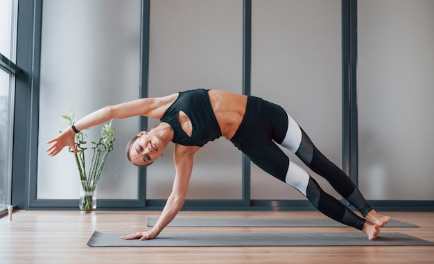 Konzentriert auf Bewegung Junge Frau in sportlicher Kleidung und mit schlankem Körper haben Fitness-Yoga-Tag drinnen