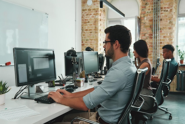 Konzentriert auf die Seitenansicht junger beschäftigter Mitarbeiter, die an Computern arbeiten, während sie sitzen