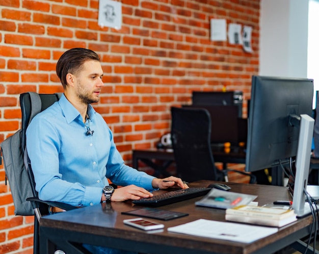 Konzentriert bei der Arbeit Selbstbewusster junger Mann in eleganter Freizeitkleidung, der am Laptop arbeitet, während er in einem Büro mit modernem Interieur sitzt