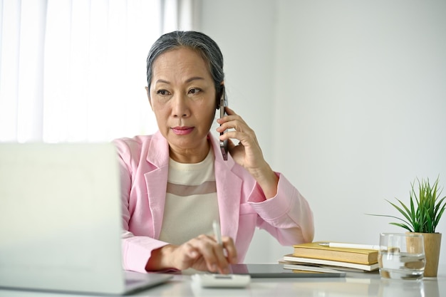 Konzentrierte ältere asiatische Geschäftsfrau spricht am Telefon