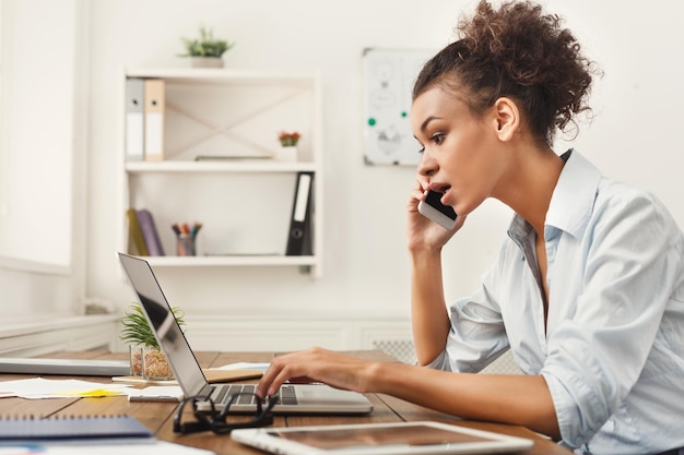 Konzentrierte afroamerikanische Geschäftsfrau bei der Arbeit, die telefoniert, an ihrem Arbeitsplatz im Büro sitzt, Platz kopieren