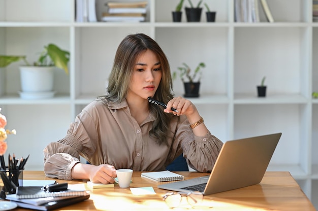 Konzentrierte attraktive Geschäftsfrau, die mit Laptop im modernen Büro arbeitet