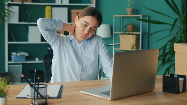 Konzentrierte Frau arbeitet an einem Tisch mit einem Laptop, der plötzlich Schmerzen im Nacken verspürt