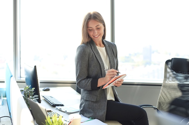 Konzentrierte junge Frau, die während der Arbeit im Büro etwas aufschreibt.