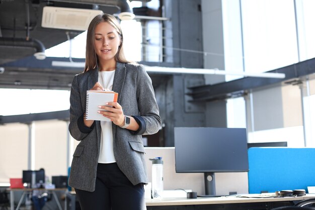 Konzentrierte junge Frau, die während der Arbeit im Büro etwas aufschreibt.