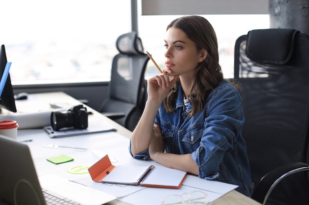 Konzentrierte junge Frau, die während der Arbeit im Büro etwas aufschreibt.