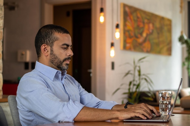 Konzentrierte junge Führungskraft im hellblauen Hemd, die am Computer im Home-Office tippt