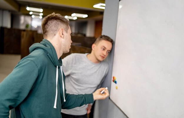 Konzentrierte Jungs stehen in der Nähe von Whiteboard Schreiben oder Lösen von Gleichungen in der modernen Halle