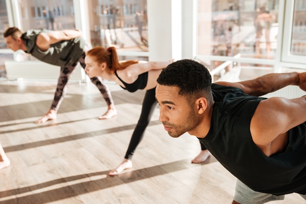 Konzentrierter afrikanischer Mann, der Yoga-Übungen in der Gruppe im Studio macht