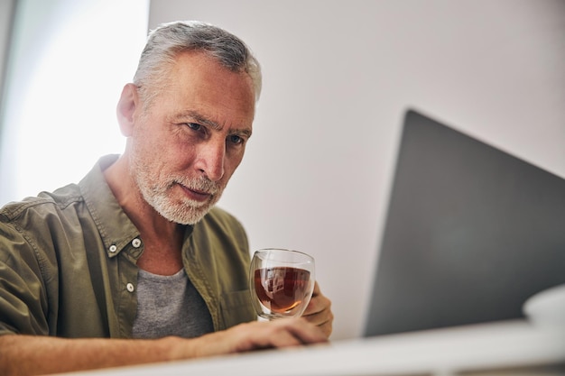 Konzentrierter alter Mann, der besorgt auf einen Laptop-Bildschirm schaut