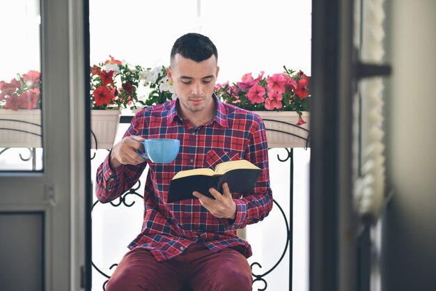 Konzentrierter bärtiger Mann, der Bücher liest und Kaffee trinkt