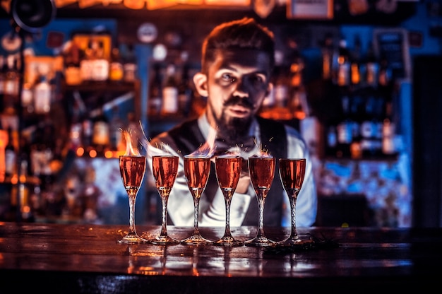 Konzentrierter Barkeeper, der frisches alkoholisches Getränk in die Gläser an der Bar gießt